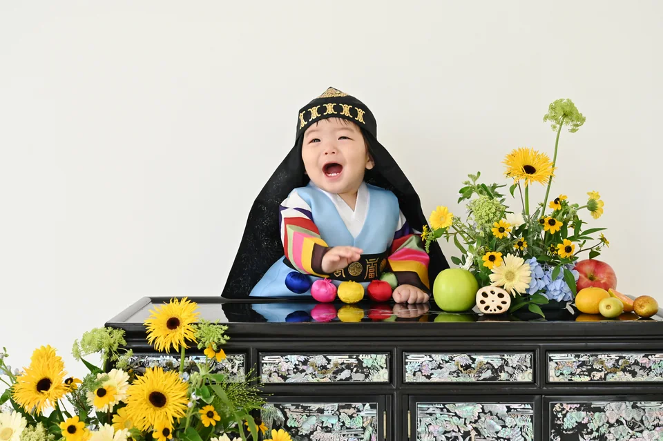 노란 꽃이 놓인 돌상 앞에서 한복을 입고 웃는 도하